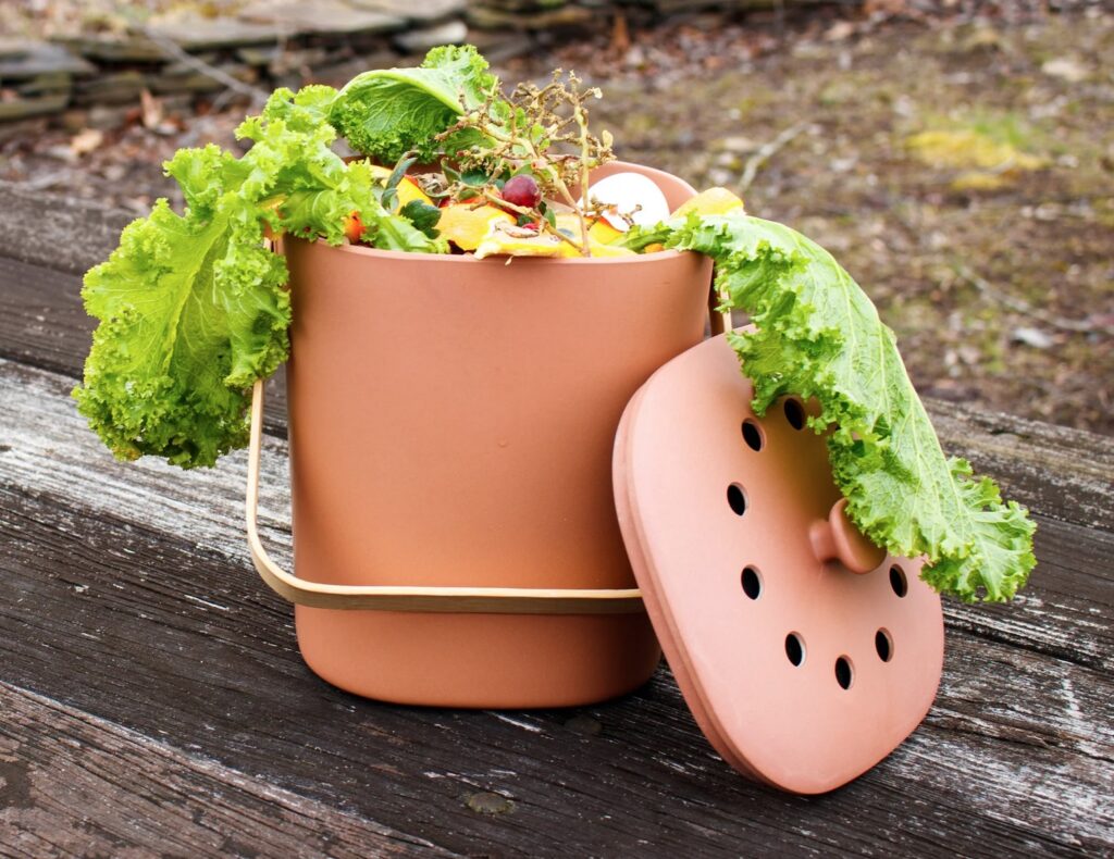Compost bin in terra cotta shown outside full of veggie scraps