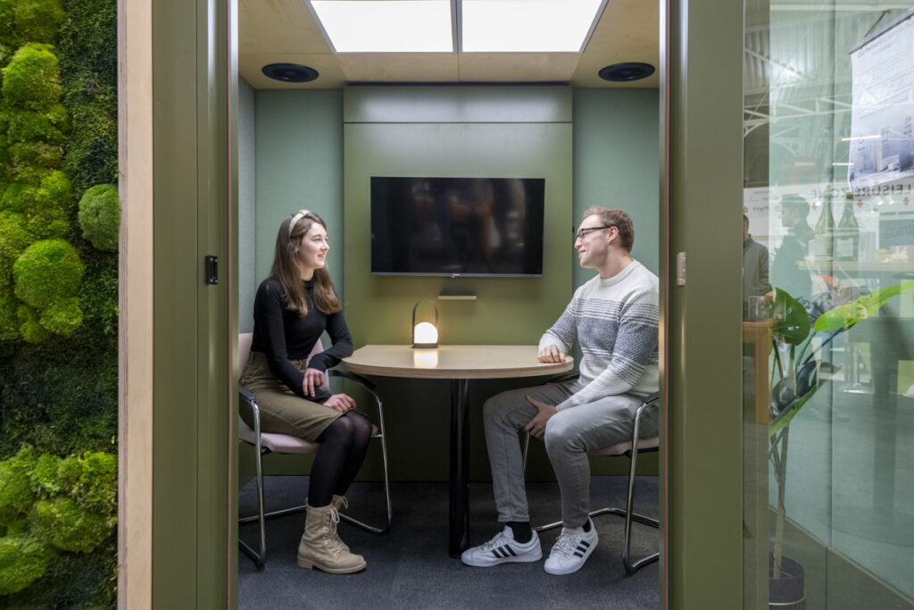 Two-person meeting room with doors open and people talking