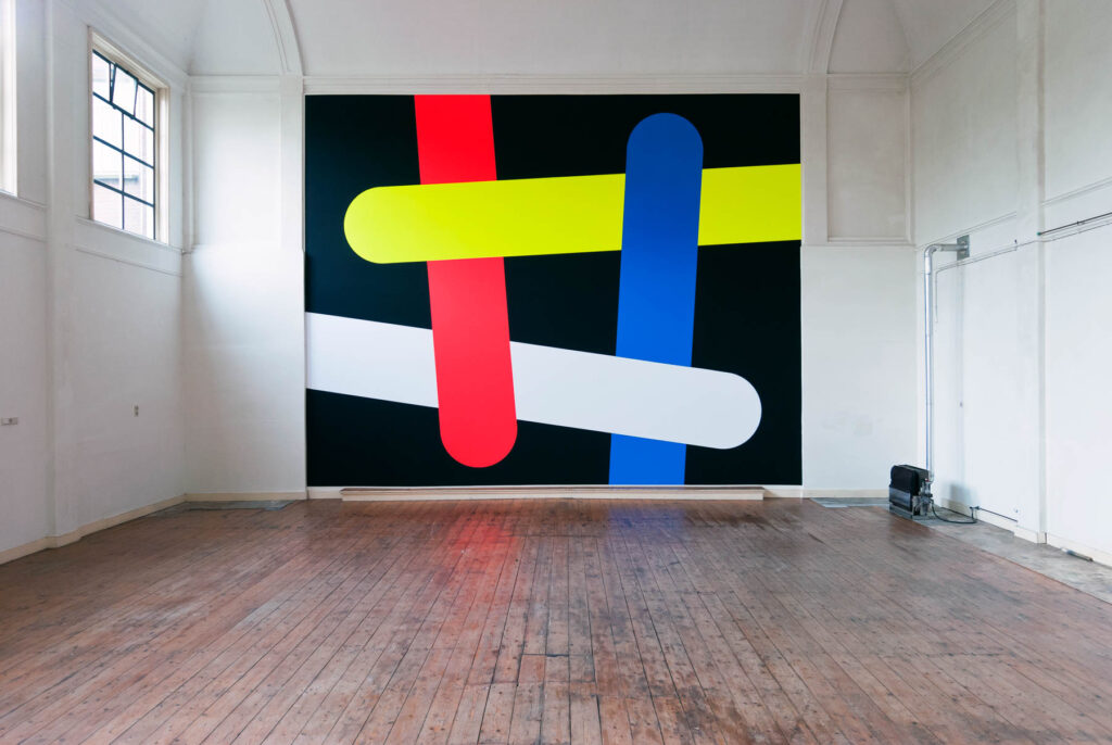 Mural in loft-like space with tongue depressor forms in vivid colors on a black background
