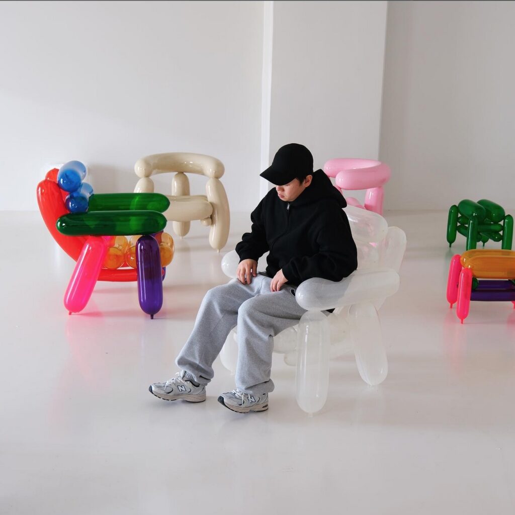 Designer seated on a transparent Blowing Series chair surrounded by other chairs