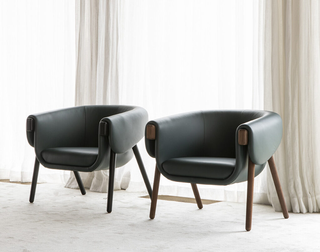 in green leather on wood leg base in front of window with curtains