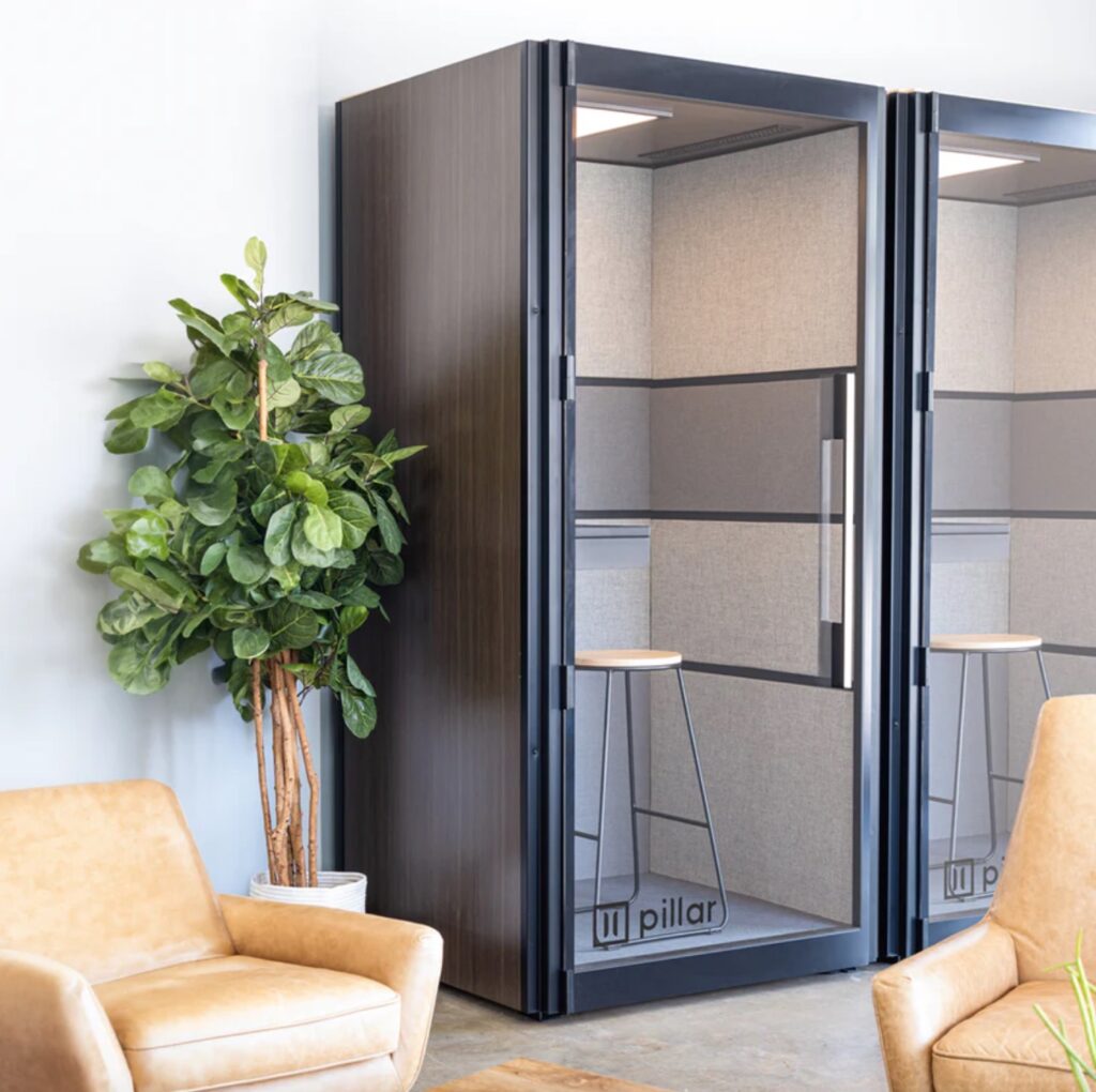 Pillar booth with dark wood exterior  and plant next to it with partial view of chairs