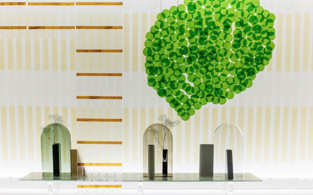 Green glass set against geometric glass elements and arched glass with ceramic vases