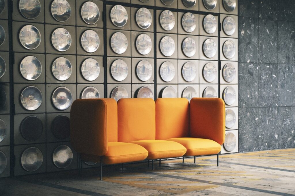 Dedas in orange against conceptual geometric wall