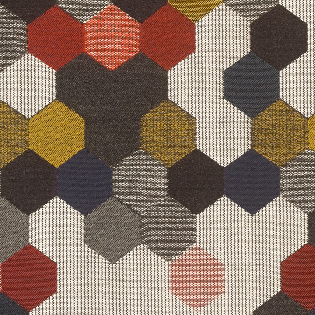Textile swatch with a repeating hexagonal motif in muted tones of red, mustard yellow, gray, and black. Each hexagon is filled with a fine mesh texture, creating a bold yet refined visual rhythm across the fabric.