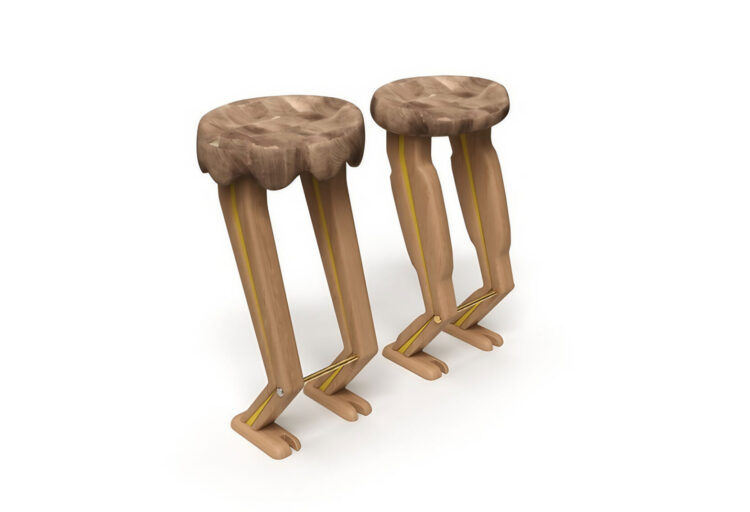 Two sculptural barstools with exaggerated leg-shaped bases carved from wood. The legs feature pointed feet, brass crossbars, and yellow detailing, while the top has a scalloped, contoured seat that adds a couture-inspired finish.