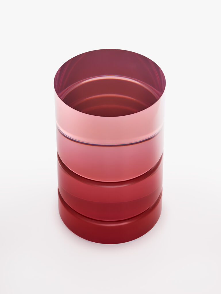 The ETS resin side table appears like a layered column of red glass, with saturated bands of pink and crimson revealing the architectural potential of cast pigment in resin.
