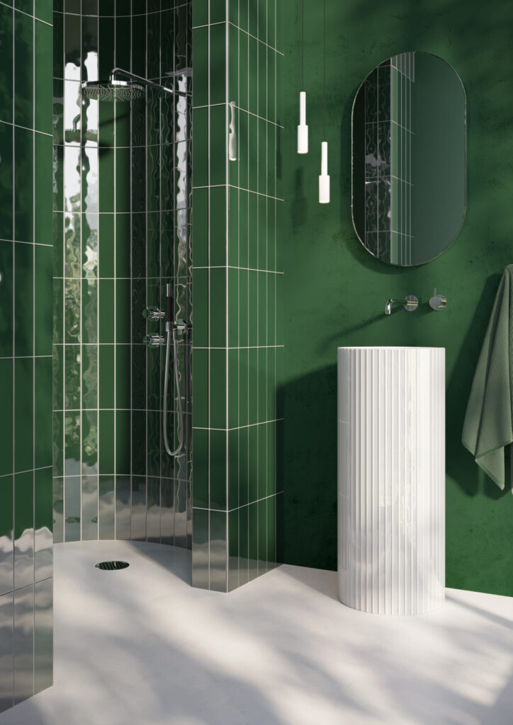 A glossy emerald-tiled shower meets a sculptural white Narciso pedestal sink, its vertically reeded glass catching the light against a minimalist matte floor.