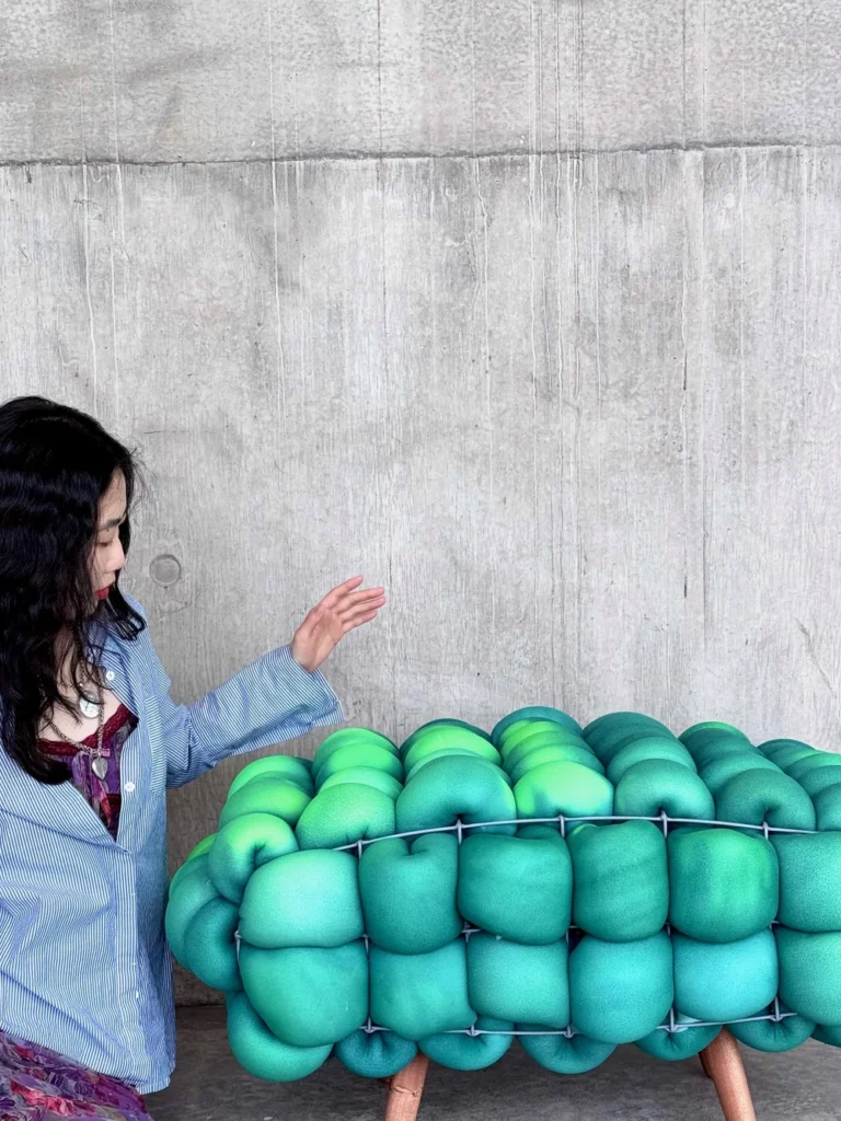 Viewer engaging with the Pangolin Series seating, where tufted foam cushions glow in green gradients as they respond to warmth.