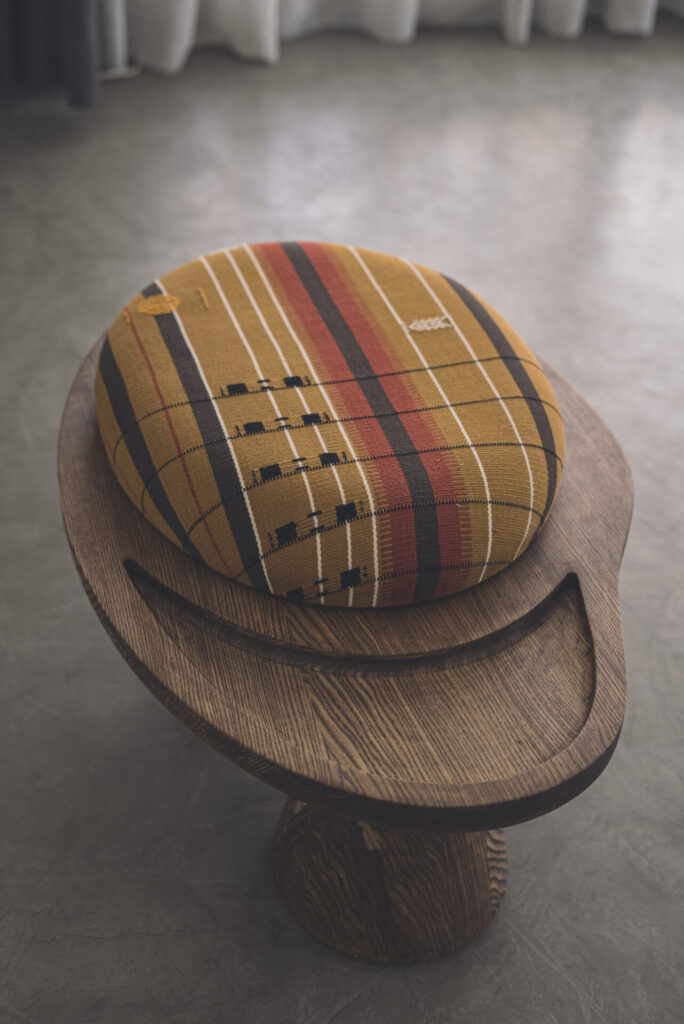 Close-up of mustard-and-rust patterned cotton ottoman seat atop a sculptural wooden base with recessed tray detail.
