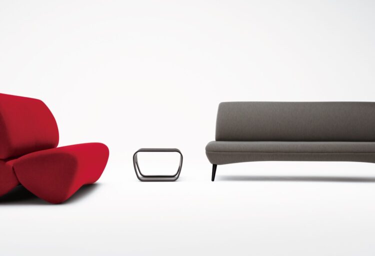 A red sculptural lounge chair with three soft, organic forms beside a minimalist brown bench and a small black side table, all on a white background.