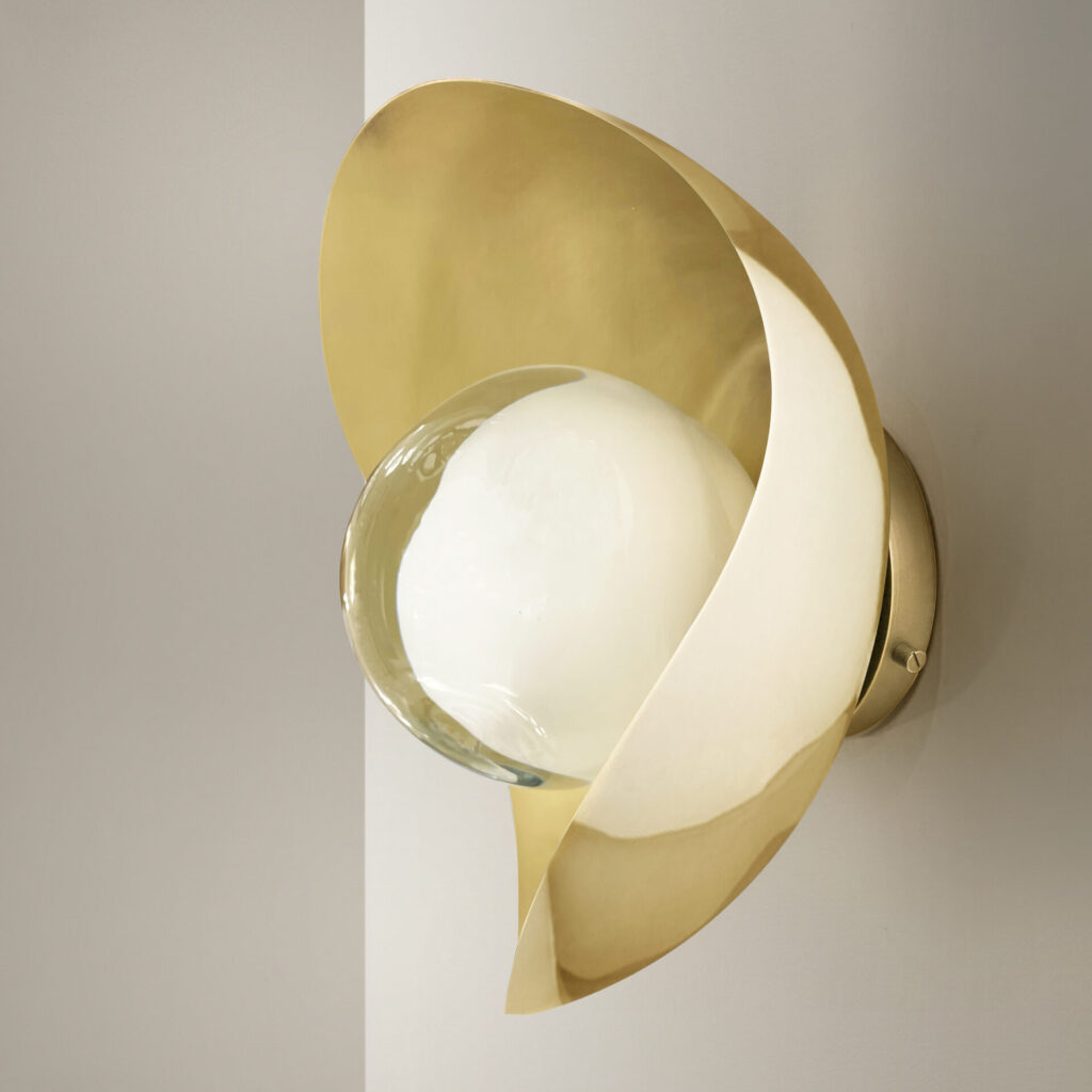 Polished brass wall sconce with a satin brass interior, featuring an asymmetrical shell that envelops a luminous glass globe.