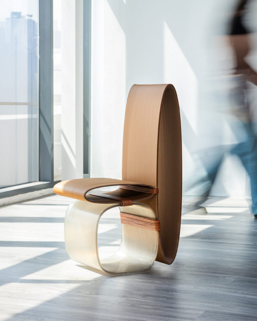 Designer assembling large-scale Stacked Modules by fastening leather bindings around curved translucent and brown components on a table.