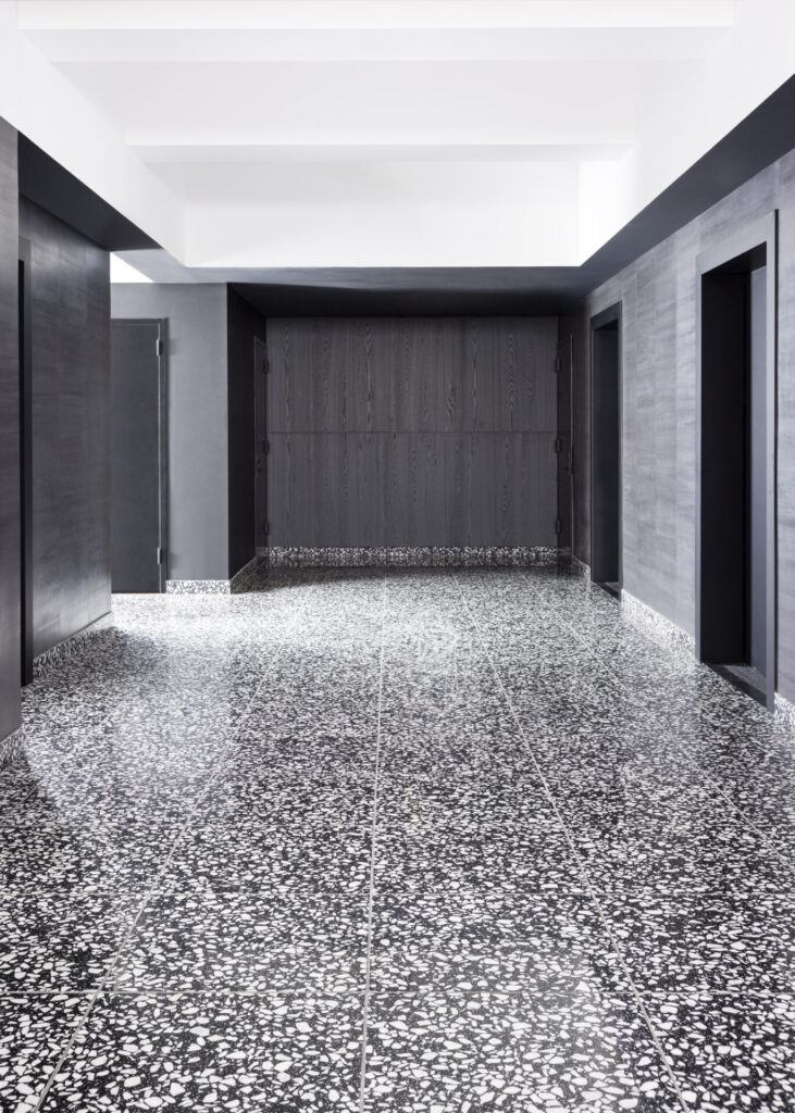 A modern office lobby with expansive Nero terrazzo flooring, where white Carrara chips shimmer against a deep black ground. The bold surface anchors the minimalist architecture, giving a polished, dramatic edge to the entry space.