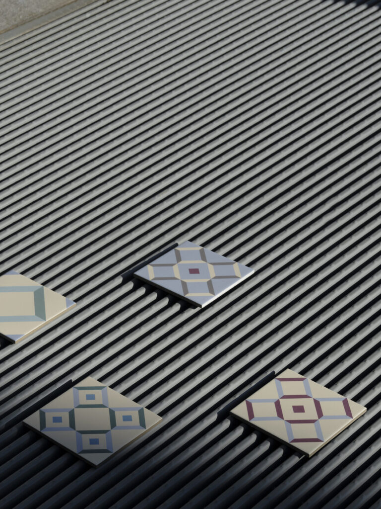 A group of Quadrille tiles arranged diagonally on ribbed metal, each with different geometric compositions in muted blues, greens, and burgundy tones.