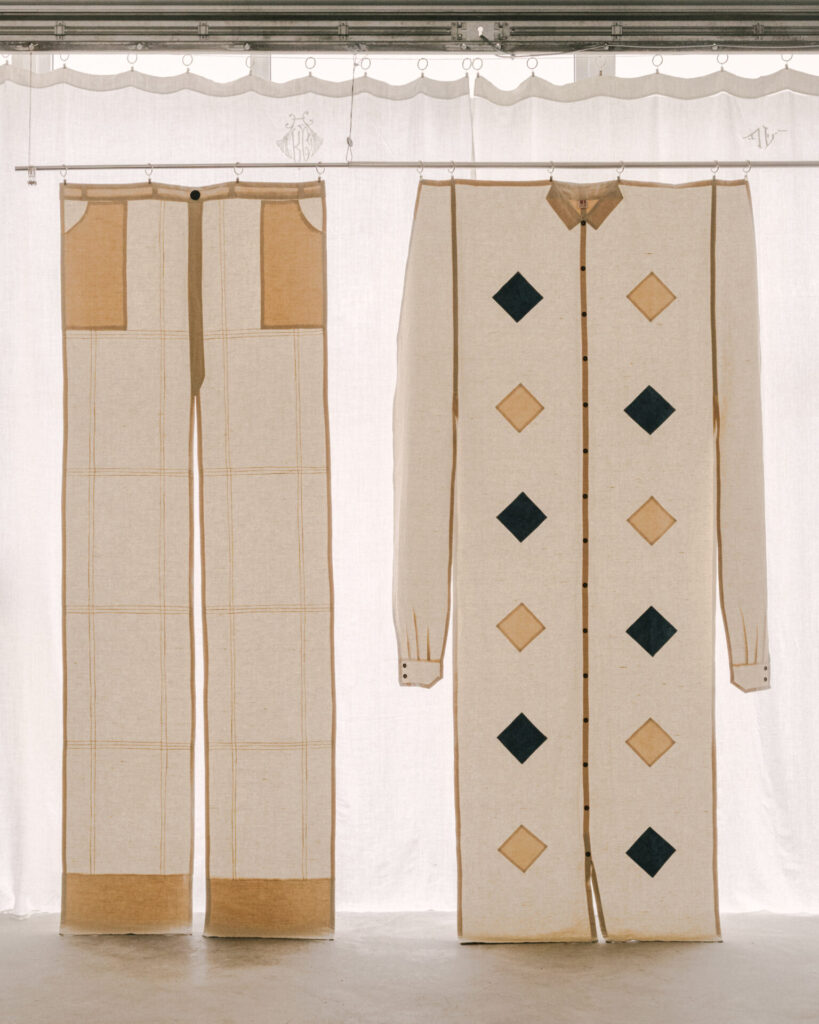 Curtains cut and stitched to mimic trousers and a patterned shirt hang together, turning functional drapery into a surreal, wearable installation in linen and wool.