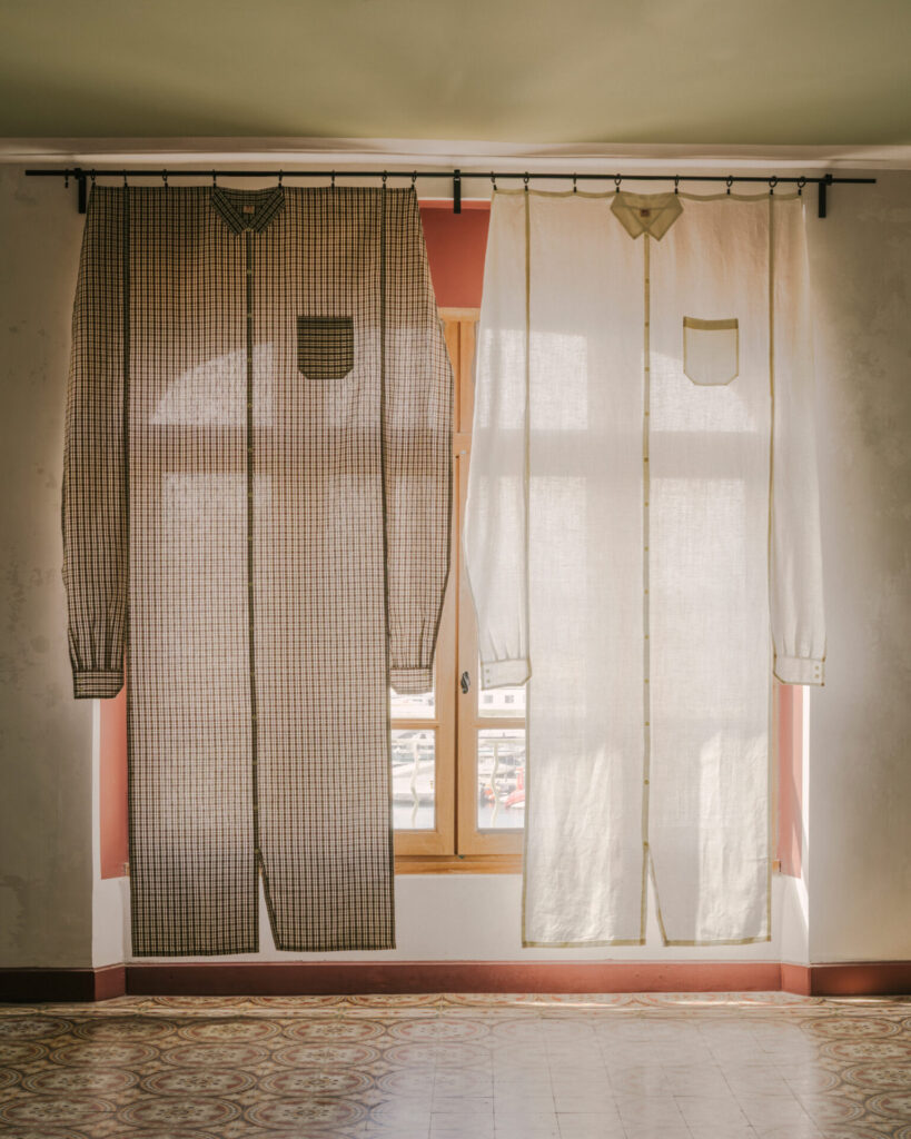 Paired curtains resembling oversized shirts—one in a checked fabric, the other in white linen—hang side by side, transforming a window into a whimsical wardrobe display.