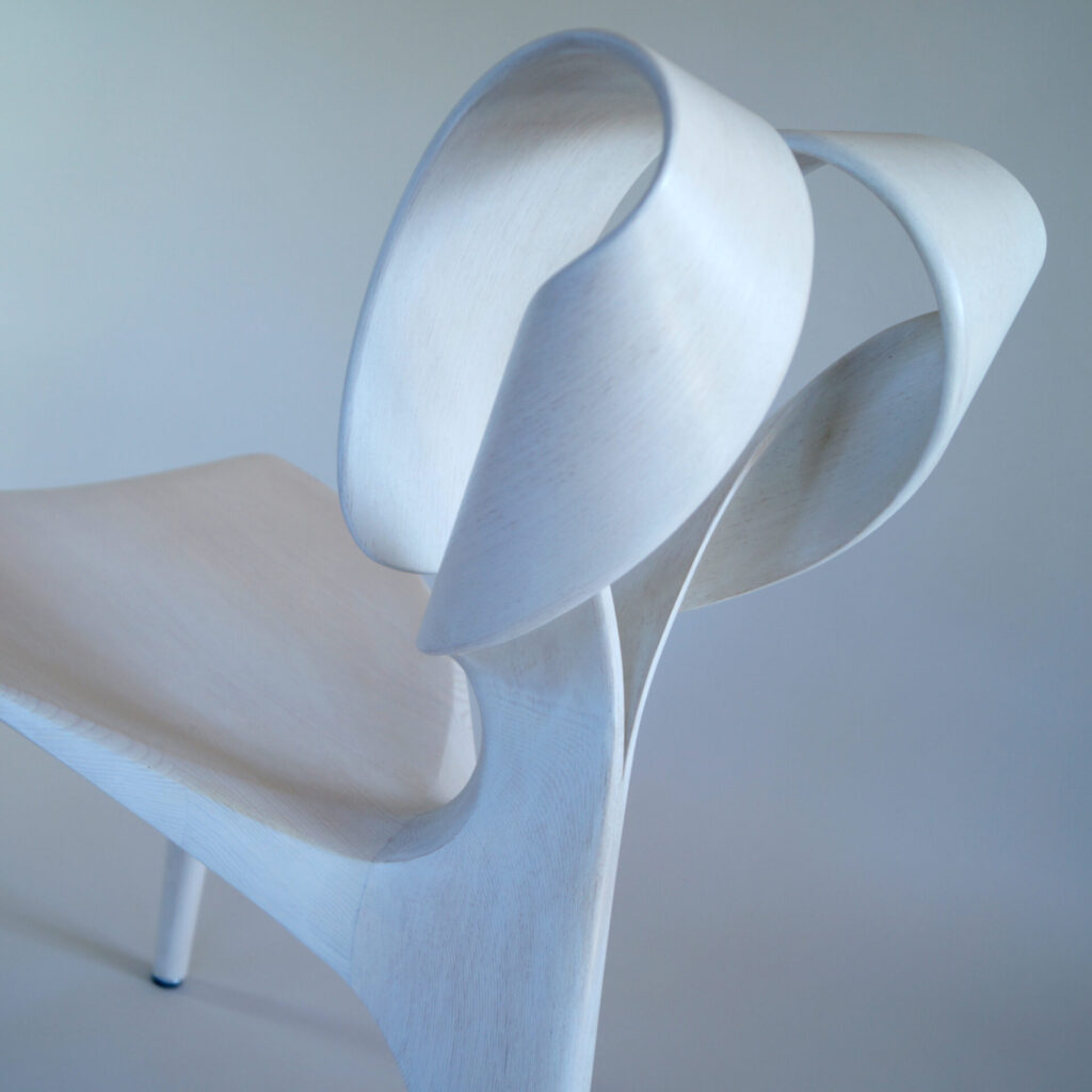 Close-up of the Aries Chair’s backrest, showing the twin loops of wood that twist gracefully from the seat, blending structure and fluid motion.