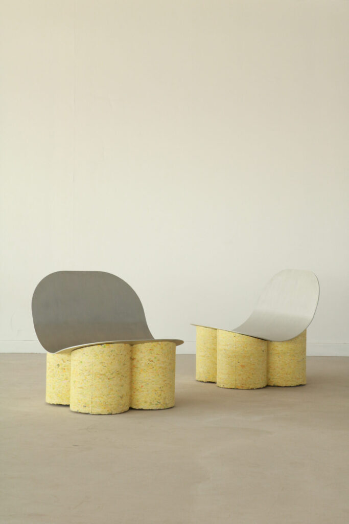 Two lounge chairs with softly curved metal seats rest on bases made from compressed yellow textile cylinders. The forms are minimal yet tactile, showing how reclaimed fabric can take on architectural strength.