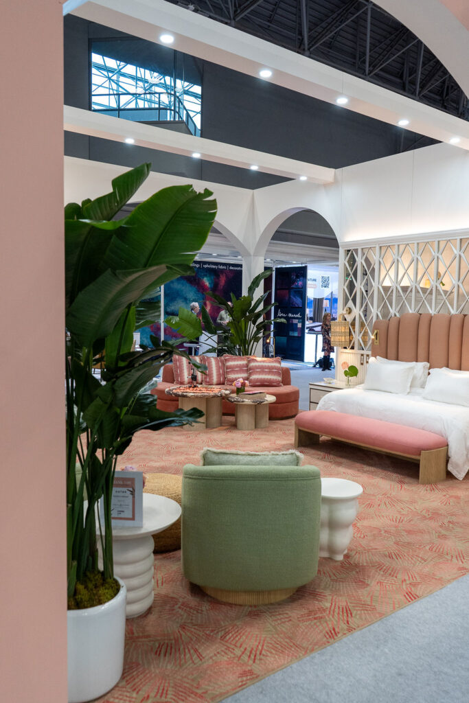 Soft greens and pinks lead into a curated lounge and bedroom setting, where rounded seating, tropical plants, and warm wood accents shape a breezy, boutique-hotel atmosphere.