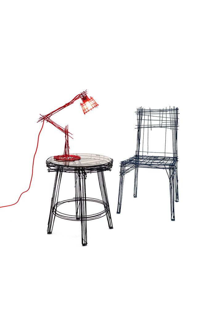 A minimalist scene of wire furniture: a black wire stool and chair paired with a red wire desk lamp, each piece resembling a hand-drawn sketch materialized in 3D.