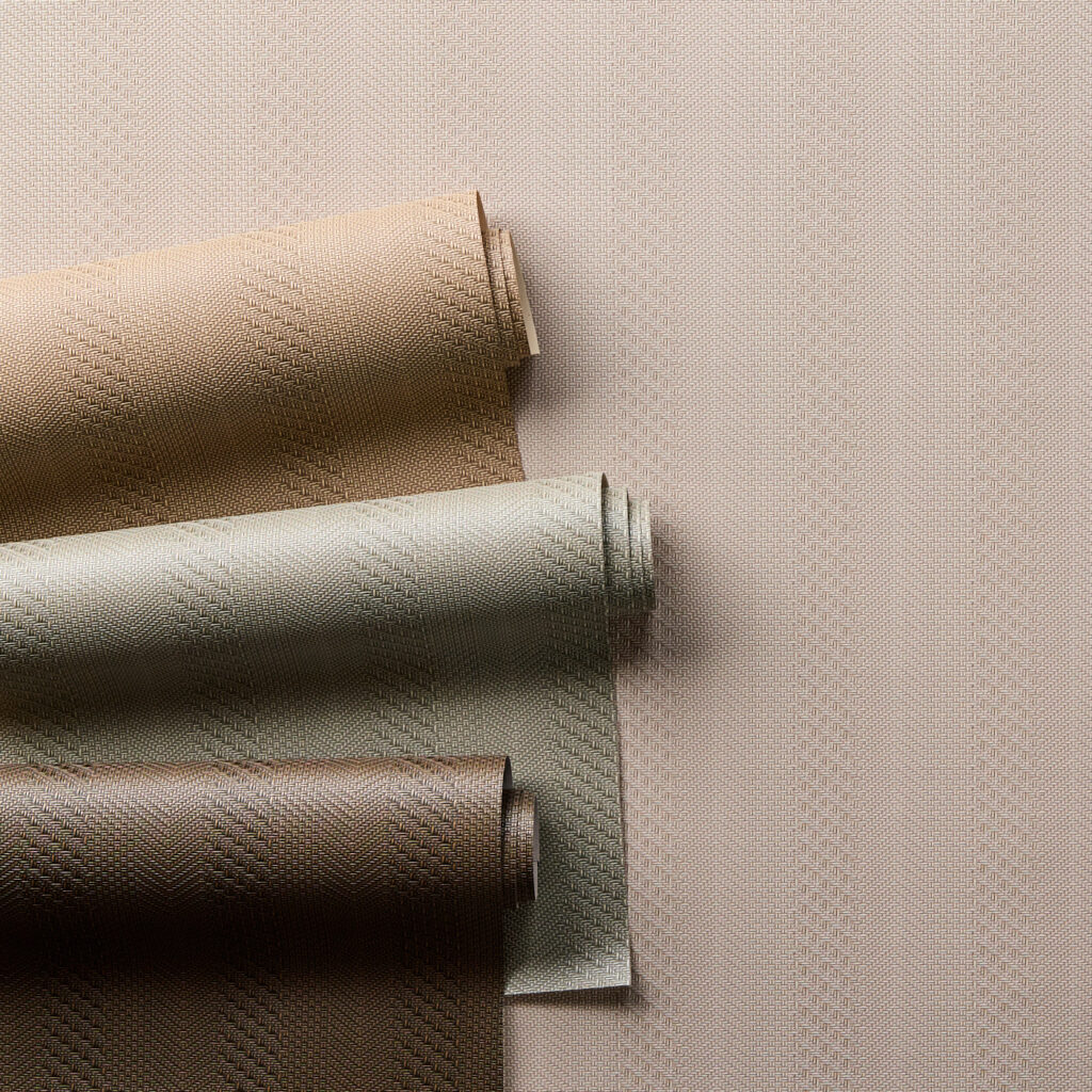 Rolled wallcoverings in warm taupe, ivory, and bronze tones reveal subtle woven geometry and light sheen, an elegant study in texture for layered interiors.