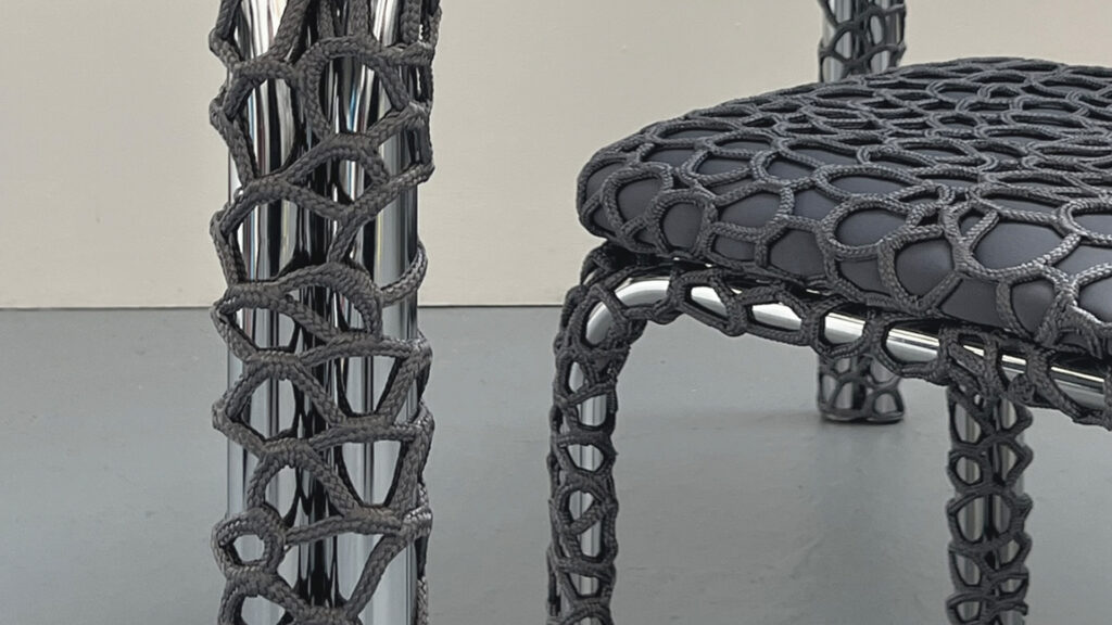 Detail of a matching chrome chair and table leg, both encased in a tight rope weave that merges craftsmanship with contemporary form.