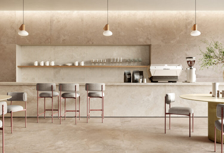 A café interior clad in warm beige porcelain tile with gentle texture. Minimal lighting and soft rose-toned furniture create a refined yet inviting atmosphere.