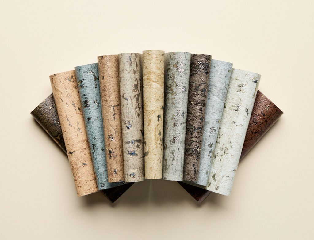 Rolled wallcoverings in warm taupe, ivory, and bronze tones reveal subtle woven geometry and light sheen, an elegant study in texture for layered interiors.