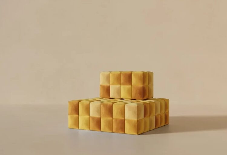 Two modular yellow poufs stack into a stepped, pixelated form, each face divided into plush squares that echo digital blocks rendered in fabric.