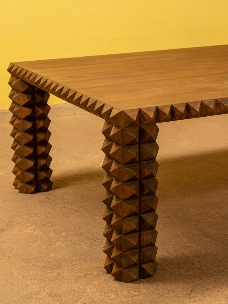 Angled view of mesa piramid revealing rhythmic wooden pyramids beneath a calm tabletop, a study in repetition and artisanal furniture design.