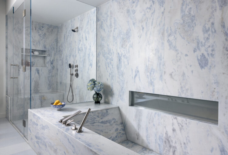 Blue Sky stone slab is carved into a sculptural soaking tub, with pale blue veining reinforcing the material’s role as both enclosure and focal point.