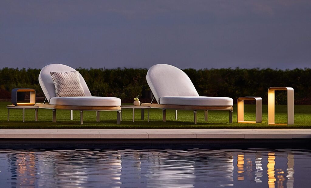 Low-profile outdoor solar lighting elements illuminate a garden setting after sunset, offering cordless flexibility and a restrained, architectural presence.