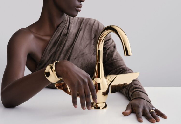 Polished gold Dornbracht VAIA faucet styled like fine jewelry, its expressive handle and high-gloss finish positioning decorative plumbing fixtures as focal elements rather than background hardware.