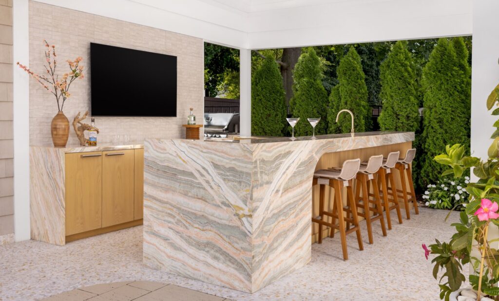 Rainbow onyx slab forms a monolithic outdoor bar, its veined stone wrapping the island with sculptural weight while anchoring the space as both surface and structure.