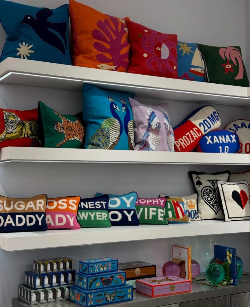 Shelving display of Jonathan Adler decorative pillows featuring bold graphics, animals, and typography at Maison&Objet 2026, illustrating playful decorative accessories for boutique retail and hospitality.