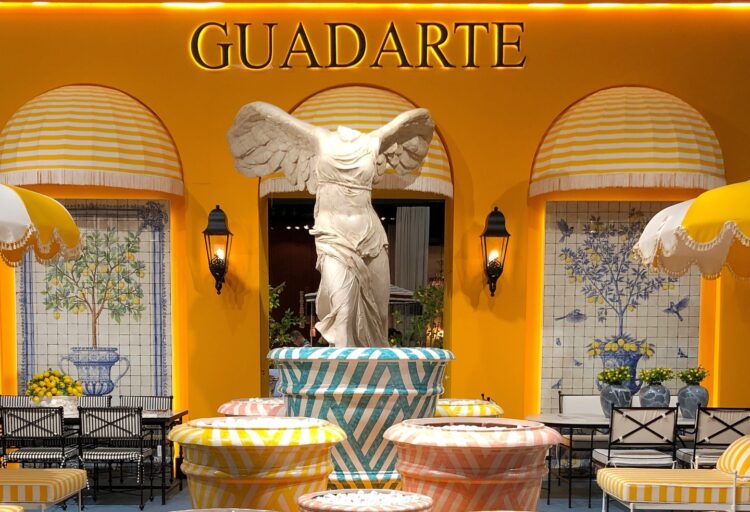Guadarte outdoor furniture display with oversized graphic ceramic planters in pastel stripes, arranged as sculptural elements beneath a classical statue.
