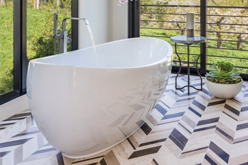 Sculptural freestanding whirlpool tub by Hydro Systems with a smooth oval silhouette, positioned near floor-to-ceiling windows above a patterned tile floor, balancing spa-level hydrotherapy with architectural restraint.