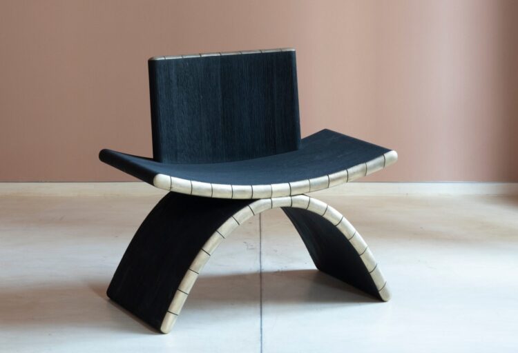 Side profile of sculptural lounge seating shown in the Tarang Chair, emphasizing the curved teak base and contoured seat form.