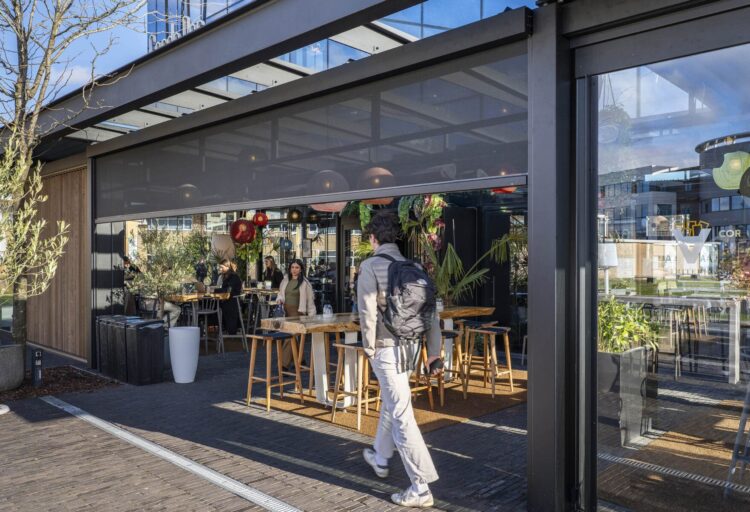Commercial terrace enclosure using Corradi Zenith retractable screens, defining a clear threshold between public circulation and protected outdoor seating.