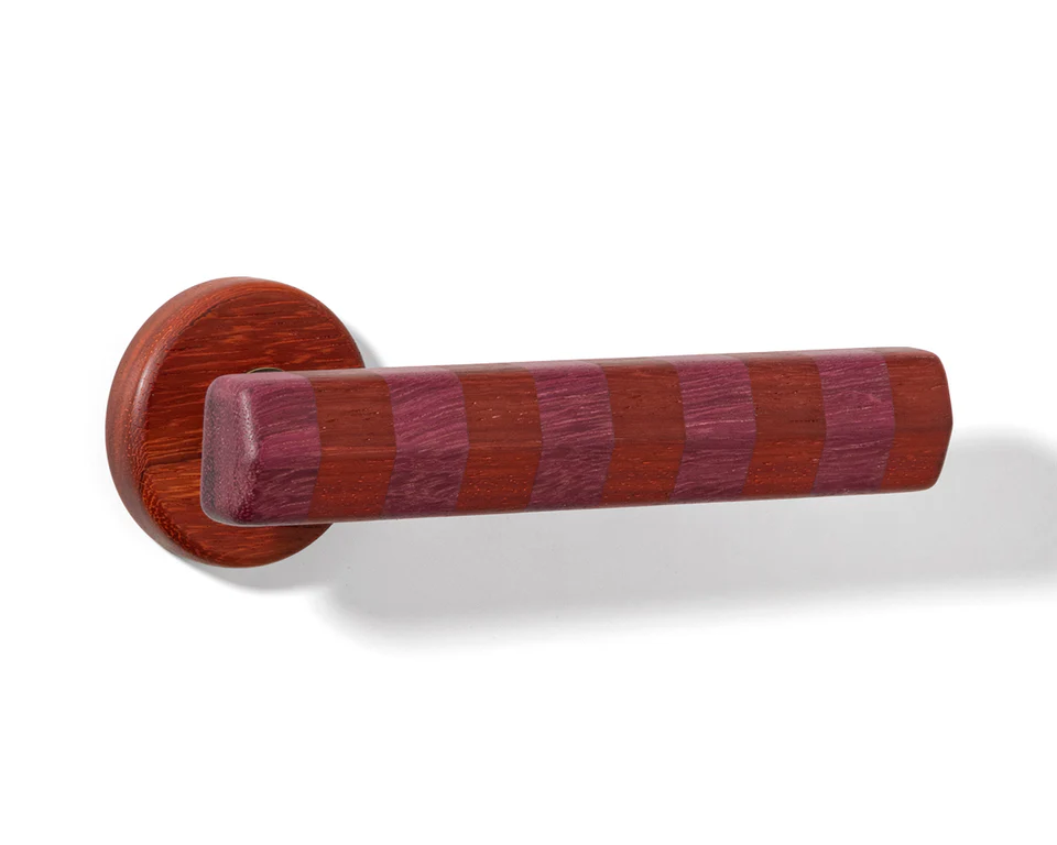 Richly colored striped timber door lever with alternating red and plum hues, demonstrating how architectural door hardware can feel both playful and grounded.