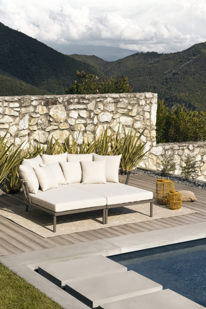 Modular Lanai daybed configuration forming a relaxed outdoor lounging island, combining woven rope structure and soft neutral upholstery within a landscaped setting.
