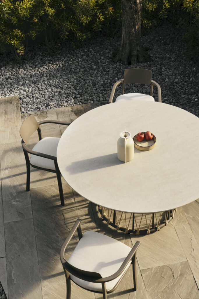 Lanai round outdoor dining table by Bizzotto with a sintered stone top and rope-wrapped base, paired with minimalist chairs in a shaded garden terrace.