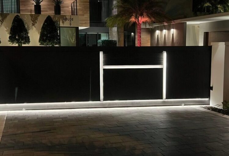 Illuminated aluminum sliding gate with embedded 3,000K LED lines glowing at dusk, transforming a residential perimeter into a sculptural architectural gate design.