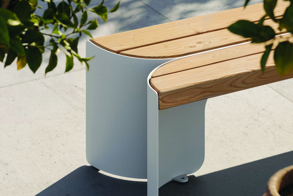 Close-up of the Floe outdoor bench by Maglin showing Douglas fir wood slats flowing into a curved steel base, emphasizing the collection’s smooth radii and refined outdoor bench seating construction.