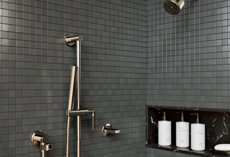 Brass shower system with knurled and smooth controls set against small grid tile, showcasing tactile kitchen and bath fixtures with a refined, mid-century edge