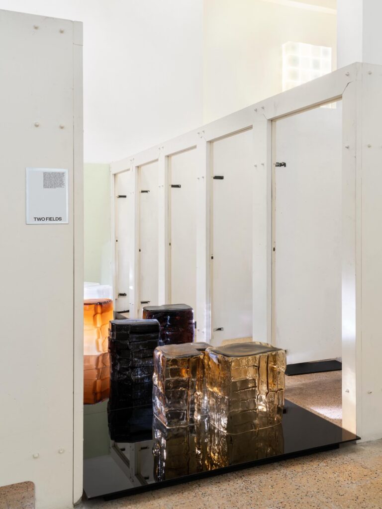 Cluster of sculptural glass stools in amber and smoked tones on a reflective platform, integrated into a larger glass lighting installation.