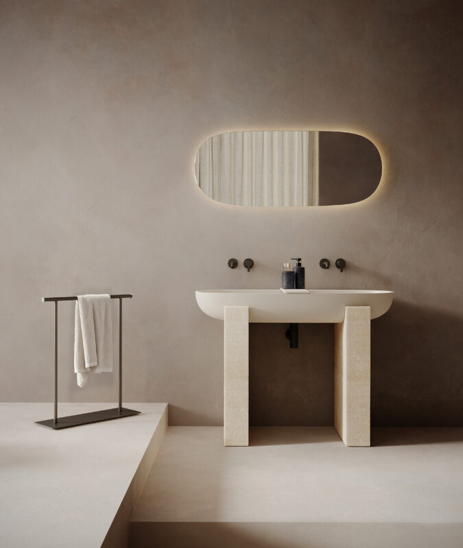 Freestanding limestone washbasin from a sculptural bathroom collection, with dual stone supports and an illuminated oval mirror against textured walls.