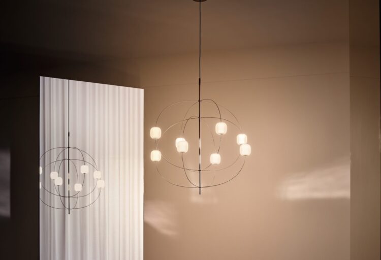 Axia chandelier installed in a minimal interior, its orbiting arms casting soft light across reflective surfaces and warm-toned walls