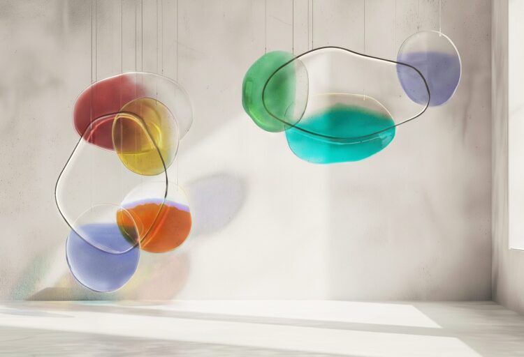 Sculptural glass lighting installation featuring multiple suspended glass forms in vibrant hues, casting soft reflections across a minimal interior wall